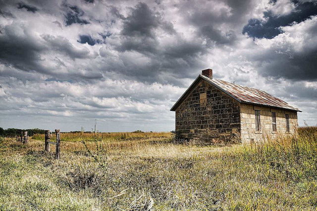 An old one-room schoolhouse in a field under a cloudy sky.